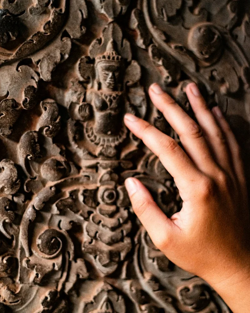Detalle de una mano sobre un panel de madera tallado con motivos ornamentales en relieve