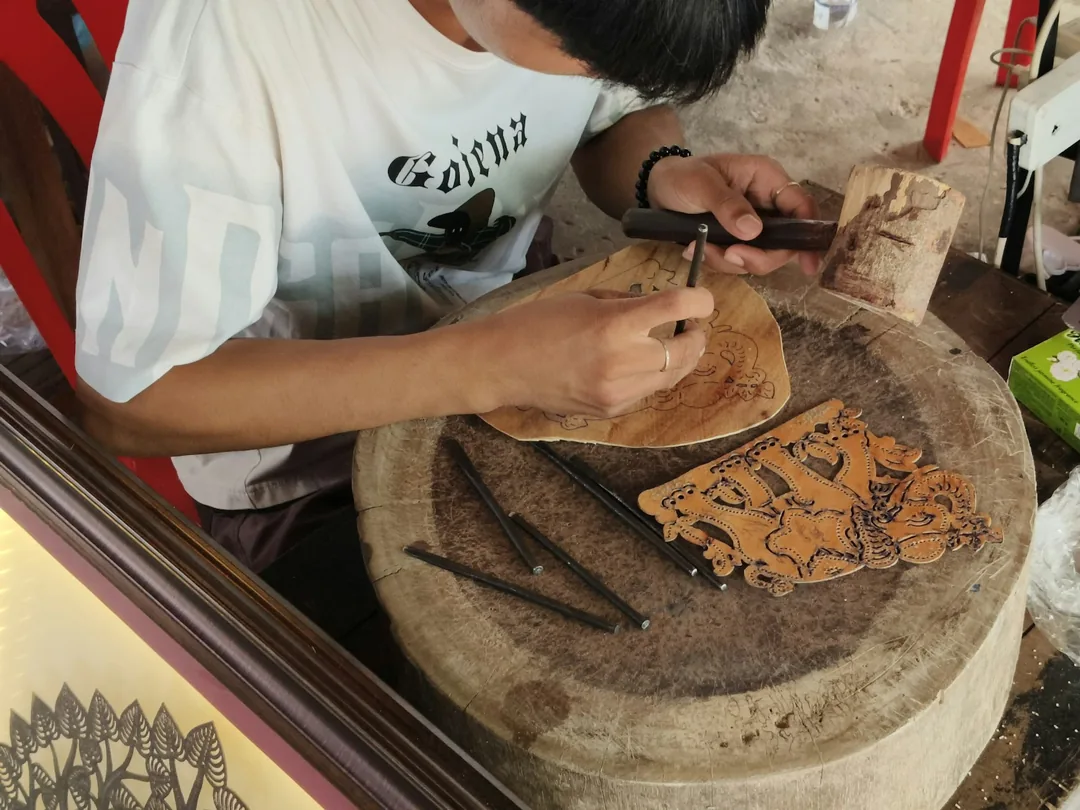 Manos trabajando una pieza de madera con herramientas tradicionales de talla sobre un banco de taller